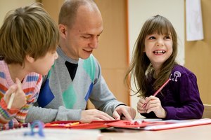 Ein BFDler sitzt mit zwei Kindern an einem Tisch und zeigt etwas in einer Unterlage, die Kinder sind interessiert nbzw. lachen.