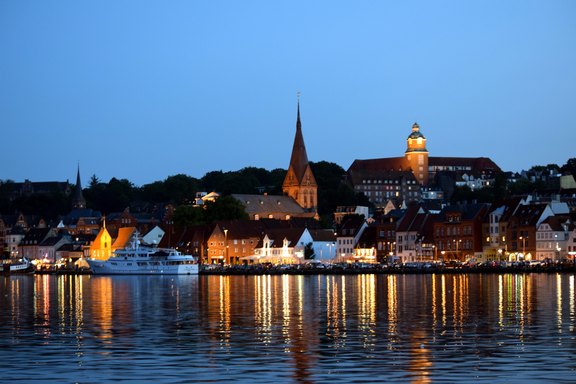 Das Bild zeigt die Stadtansicht von Flensburg vom Wasser aus bei abendlicher Stimmung.