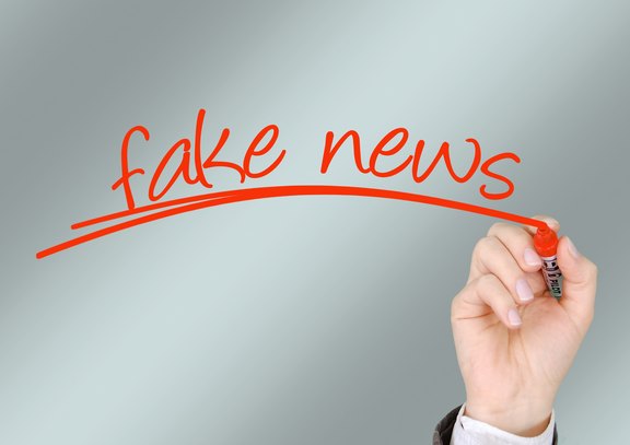 Eine Hand schreibt mit einem Roten Stift auf eine Glasscheibe "Fake News"