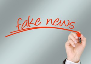 Eine Hand schreibt mit einem Roten Stift auf eine Glasscheibe "Fake News"
