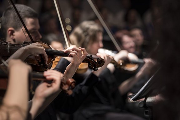 Man sieht auf dem Bild mit einer Reihe von Geigenspielenden Teil eines klassischen Orchesters