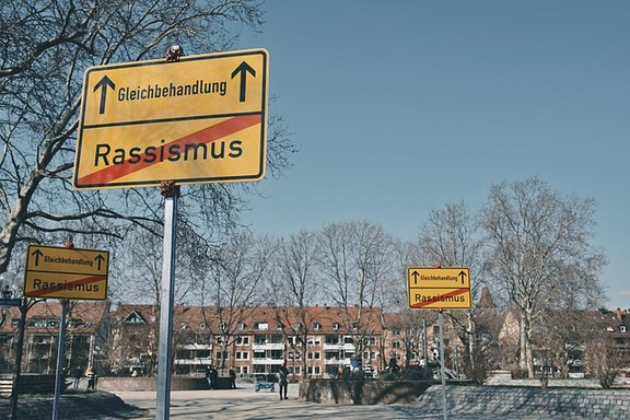 Stadtbild mit gelben Straßenschildern, auf denen das Wort Rassismus durchgestrichen ist.