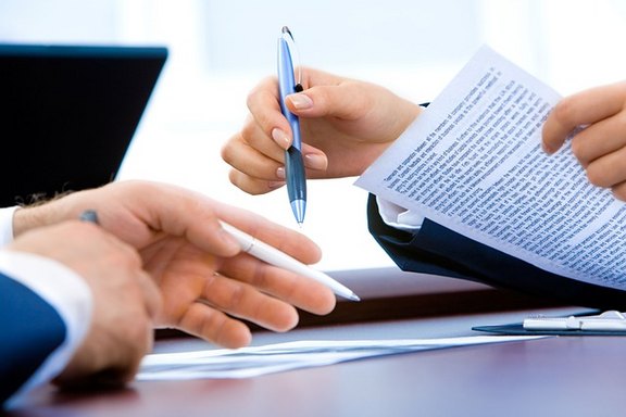 Zu sehen sind die Hände von zwei Personen, die sich gegenüber sitzen, eine hat Stift und Papier in der Hand.