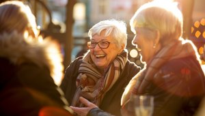 Zwei Seniorinnen und eine weitere Person stehen in der Abendsonne und unterhalten sich gutgelaunt.