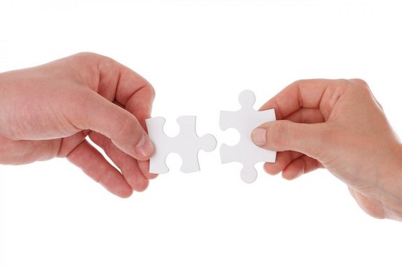 Zwei Hände halten zwei weiße Puzzleteile, die zueinander passen könnten.