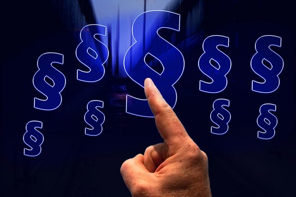 Mit einem Zeigefinger wird auf eine Reihe von Paragrafenzeichen in blauer Farbe gezeigt. Der Hintergrund ist schwarz.