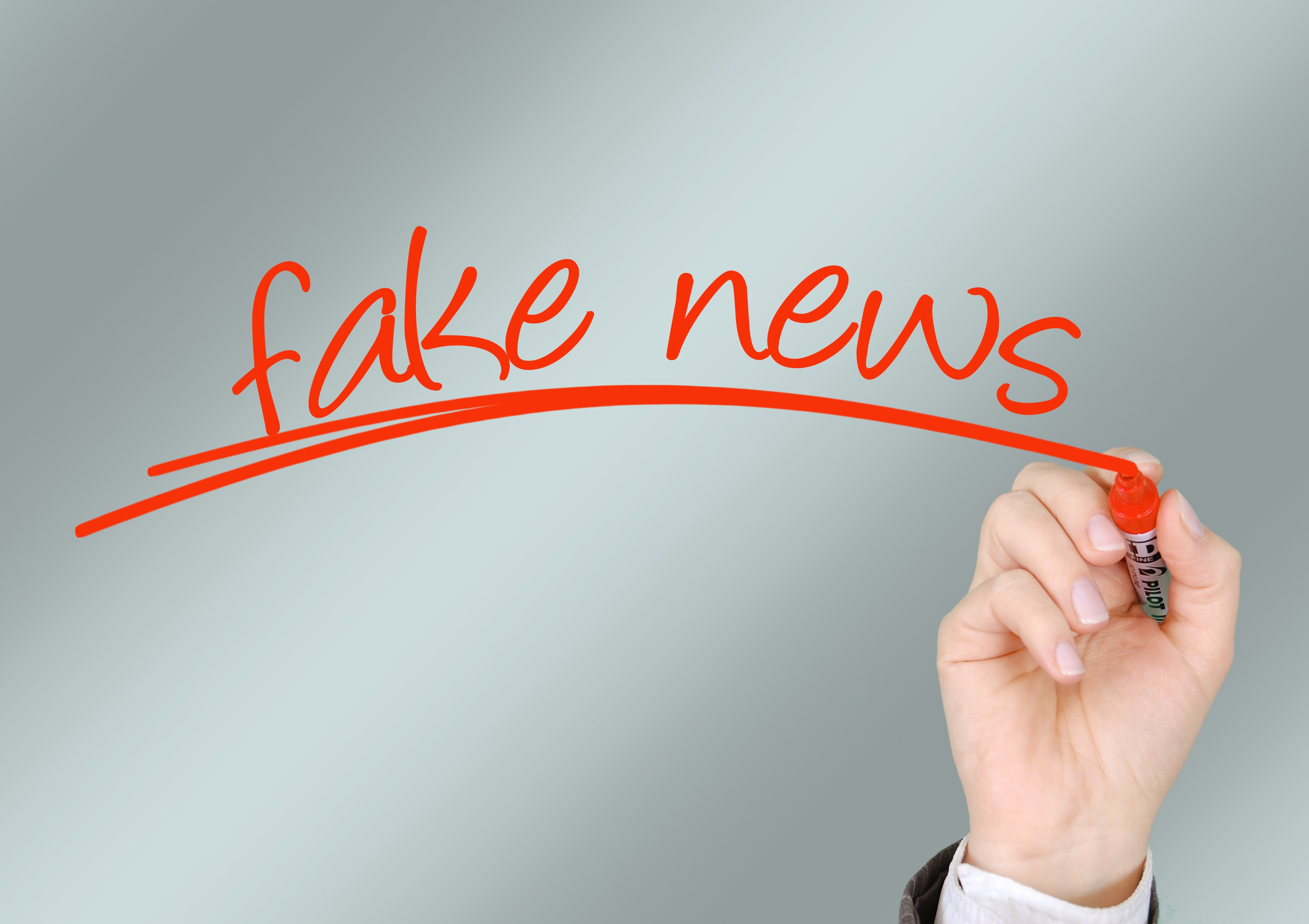 Eine Hand schreibt mit einem Roten Stift auf eine Glasscheibe "Fake News"