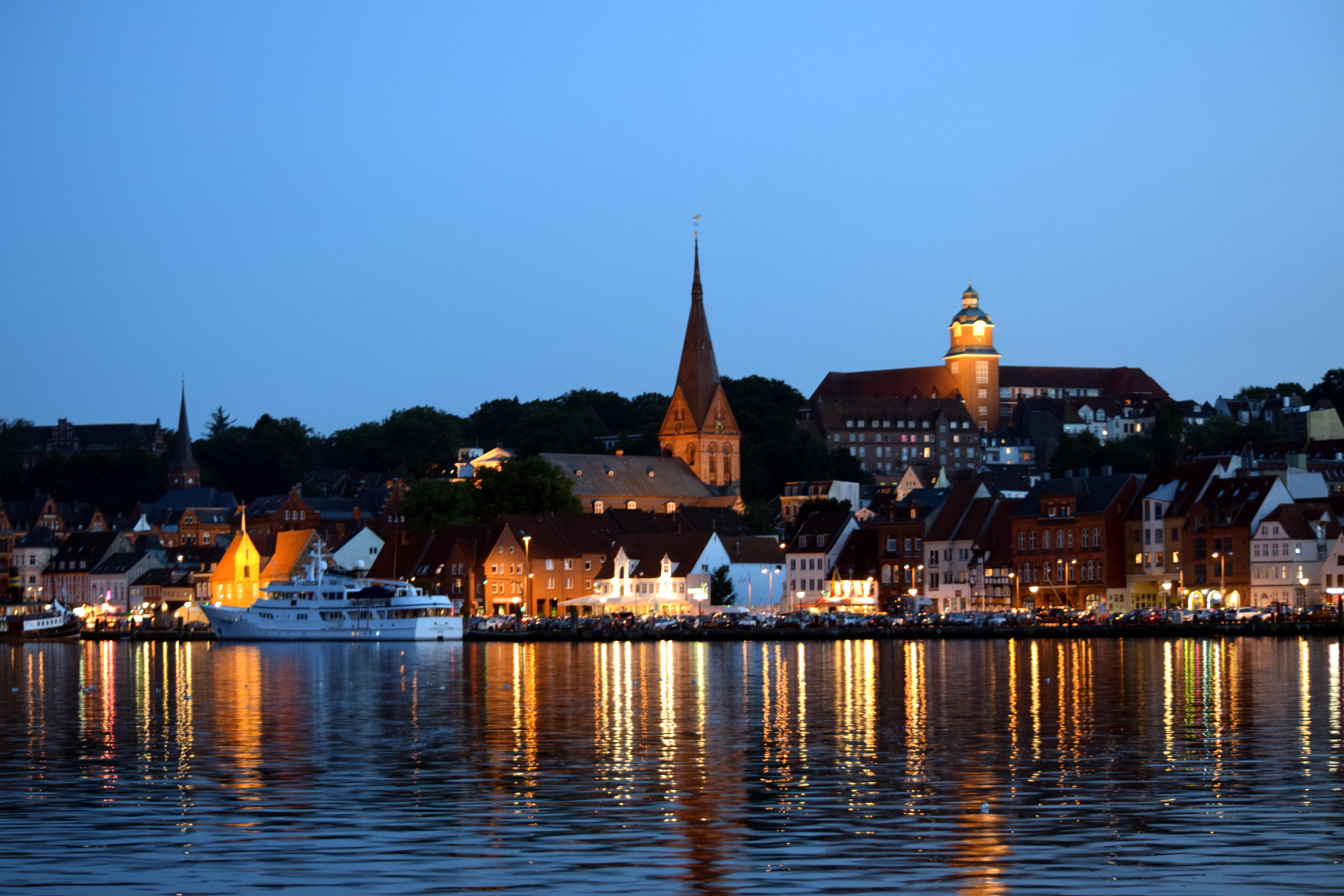 Das Bild zeigt die Stadtansicht von Flensburg vom Wasser aus bei abendlicher Stimmung.