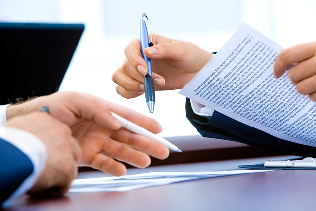 Zu sehen sind die Hände von zwei Personen, die sich gegenüber sitzen, eine hat Stift und Papier in der Hand.