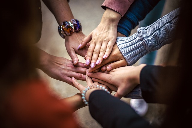 Eine Gruppe unterschiedlicher Menschen legen jeweils eine Hand in der Mitte des Bildes auf die Hände der anderen der Gruppe.